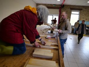 Projet Nos Cabanes © William Windrestin / visuel de deux personnes en premier plan qui mesurent et découpent du bois