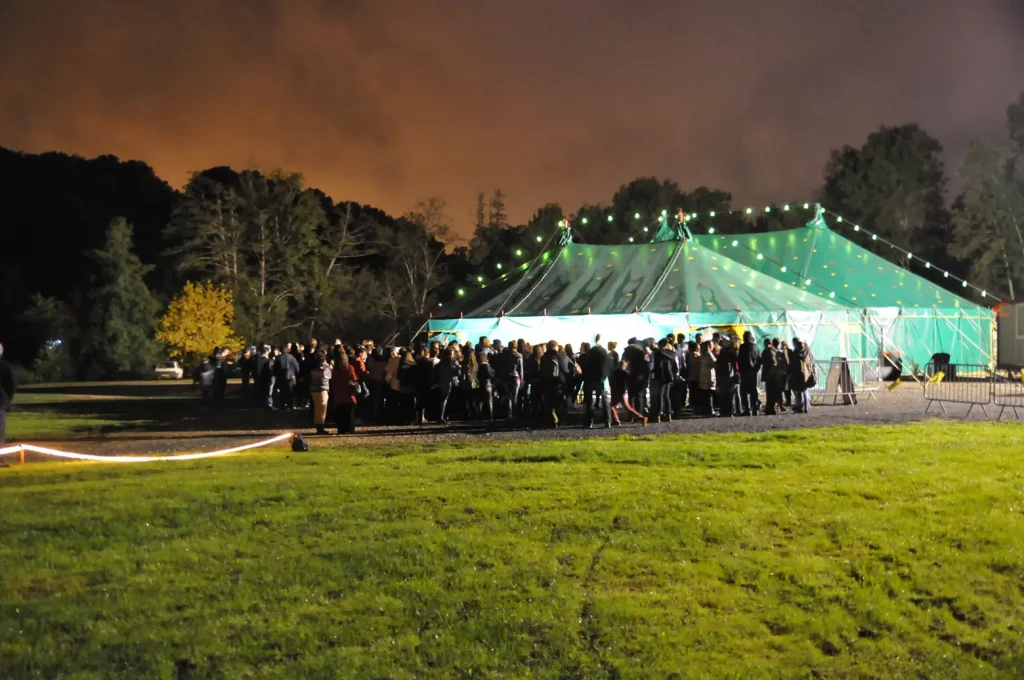 Visuel qui représente un chapiteau de nuit et un public à l'extérieur